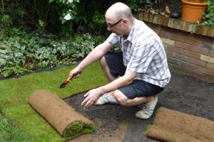 Laying a roll of turf against existing lawn and the edging, note had tool